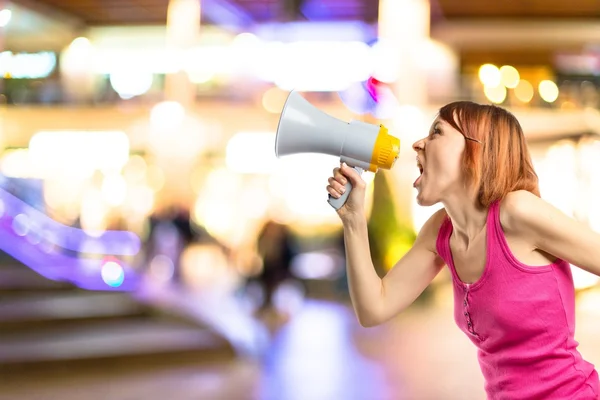Redhead girl shouting with a megaphone over white background