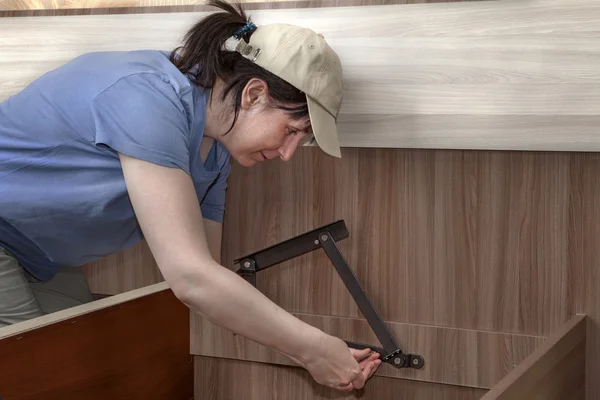 Woman assembles furniture, hinges lifting system screwed to bed frame.