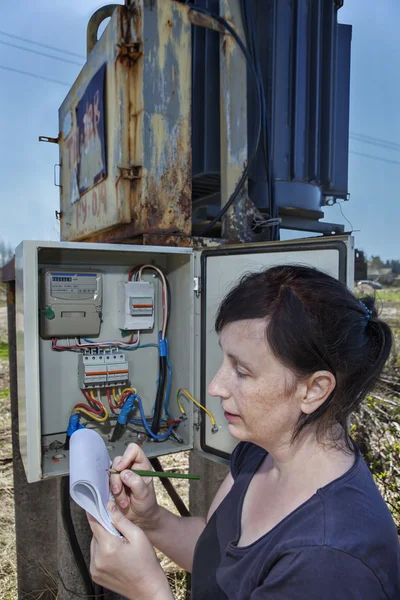 Woman technician inspecting electric meter reading  in distribution switchgear, outdoors.