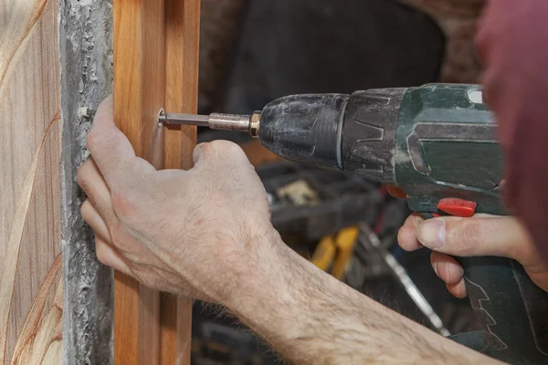 Woodworker screwed jamb in doorway using cordless drill electric screwdriver.