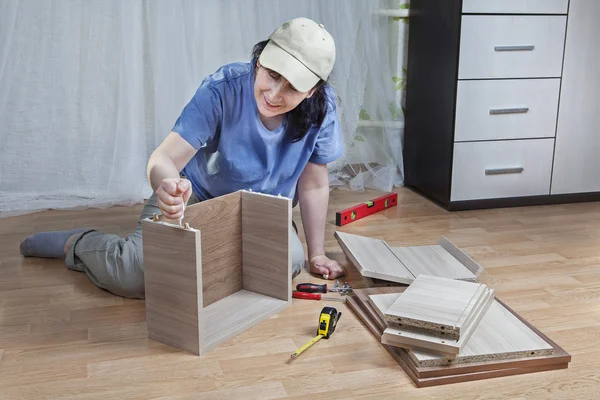 Assembling of furniture, woman mounts box of chipboard, using glue
