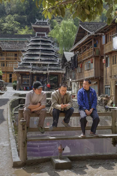 Dong minority village, three Chinese rest on bench, Guizhou, China.