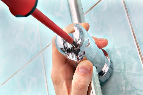 Close-up plumbing hand with screwdriver, adjust angle of shower holder.
