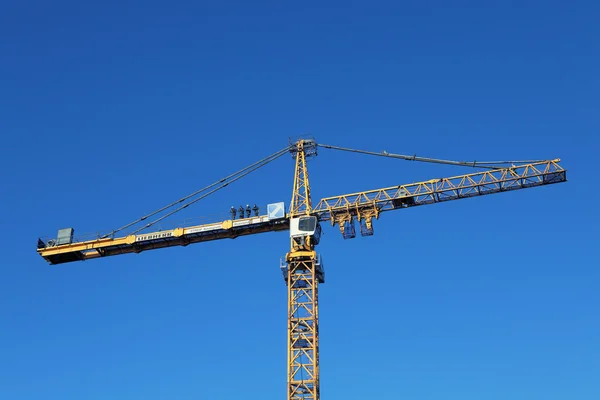 Team of installers stands on counterweight jib yellow tower crane.