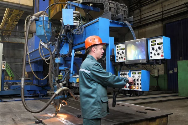 Working operator controls welding robot, standing at control panel