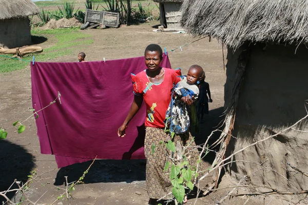 Maasai village, dark-skinned woman holds a child.