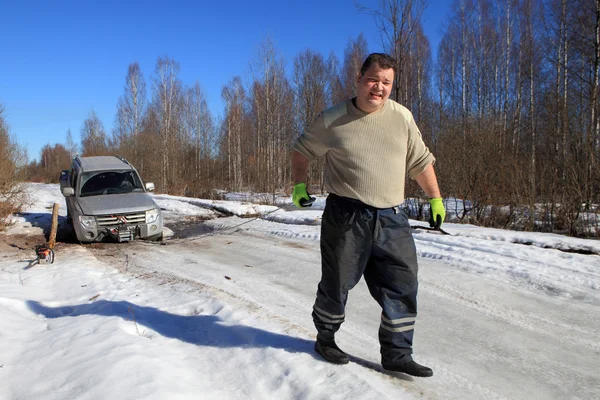 Car stuck on forest road, man pulls cable automotive winch.