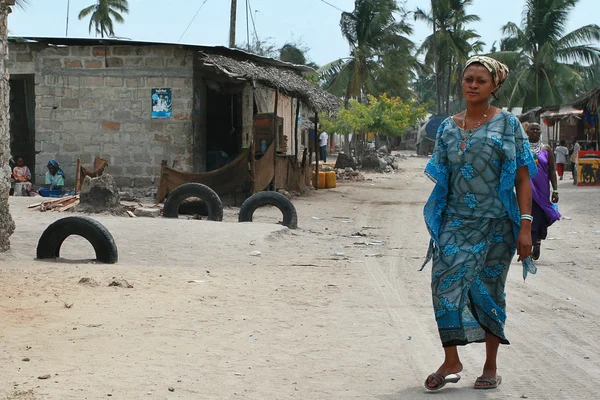 African woman walking on dirt road of coastal fishing village.
