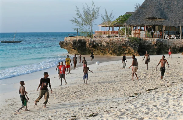 African teenagers playing beach football on shores of Indian Ocean.