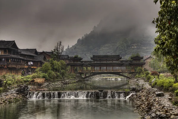 Dam on rural river and covered carved wooden bridge, China.