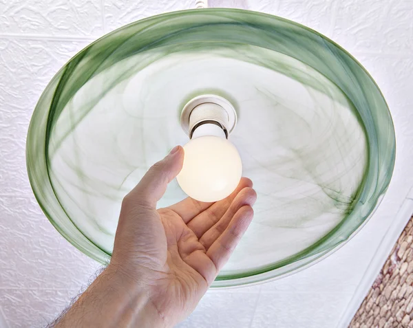 Hand twists energy-saving LED lamp on ceiling light.