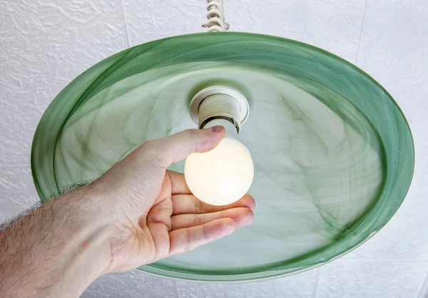 Human hand twists LED lamp into ceiling fixture green glass.