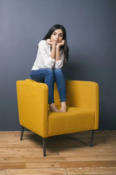 Calm black-haired girl sitting on chair back with face leaning on hands