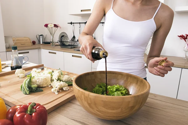 Unrecognizable woman adding soya sauce in salad in bowl