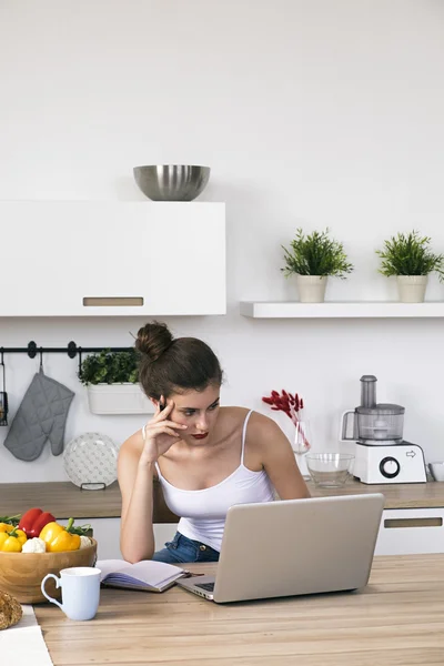 Pensive woman working on laptop in kitchen