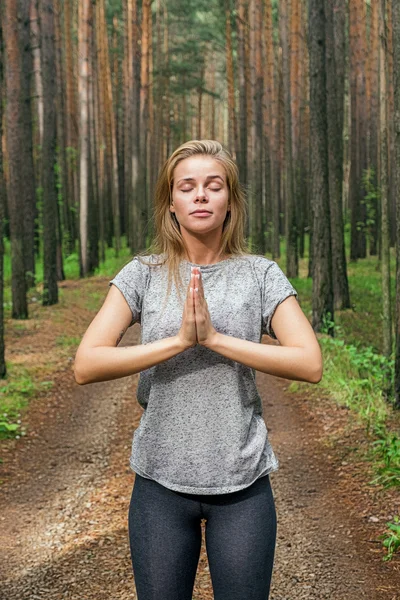 Blonde girl with eyes closed with hands in namaste in forest