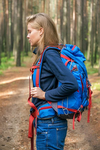 Side view of young blonde girl with blue backpack in forest