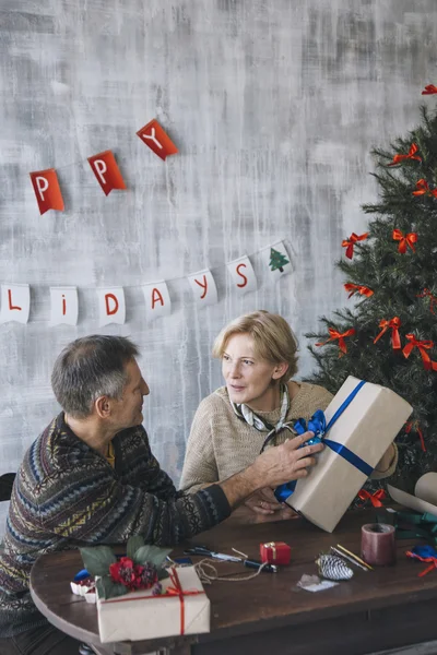 Couple of elderly people talking while holding decorated Christmas present