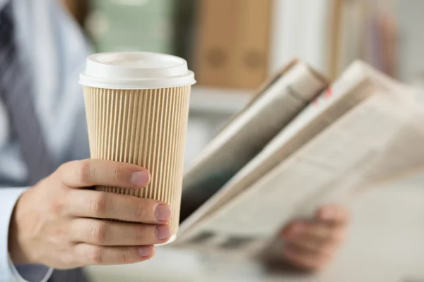 Closeup of businessman reading news and holding coffee cup