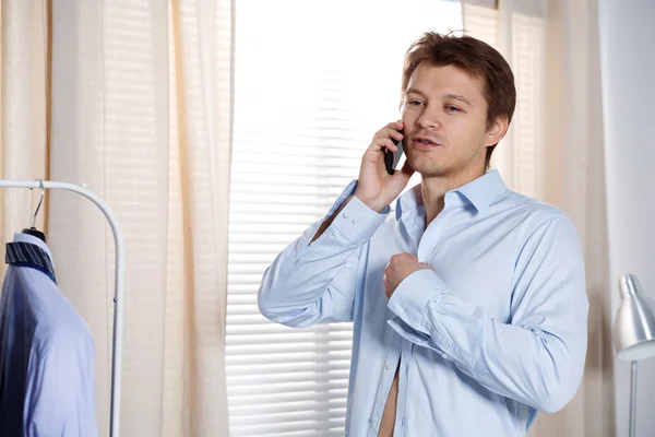 Portrait of busy young man putting on his shirt and talking on p