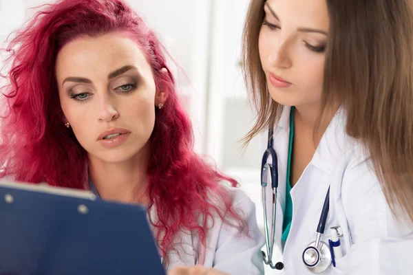 Two female doctors looking at clipboard with patient information