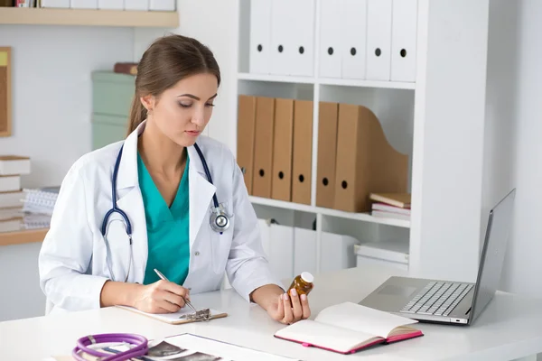 Female medicine doctor holding bottle with pills and writing pre