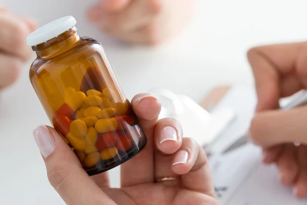 Close-up view of female doctor\'s hand holding bottle with pills