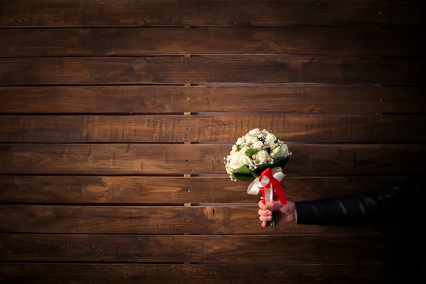 Wedding bouquet of white roses in groom\'s hand on wooden wall