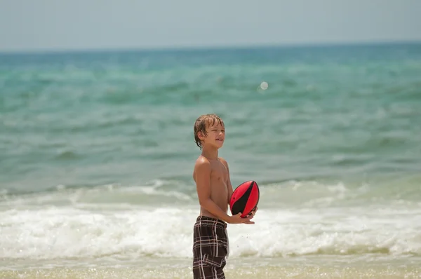 Cute little boy catching football on beach.