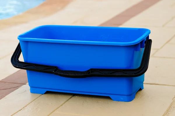 Blue plastic bucket sitting outdoors on concrete patio.