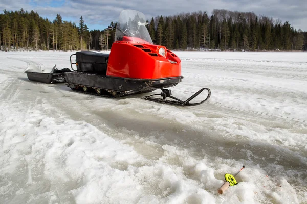 During winter fishing rod lies on the ice near the snowmobile