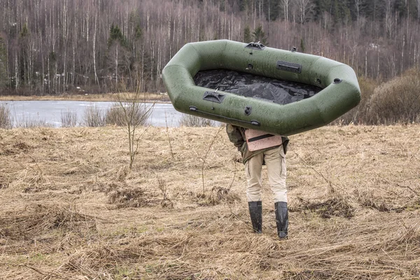 Man carries a rubber inflatable boat on the shore of the lake