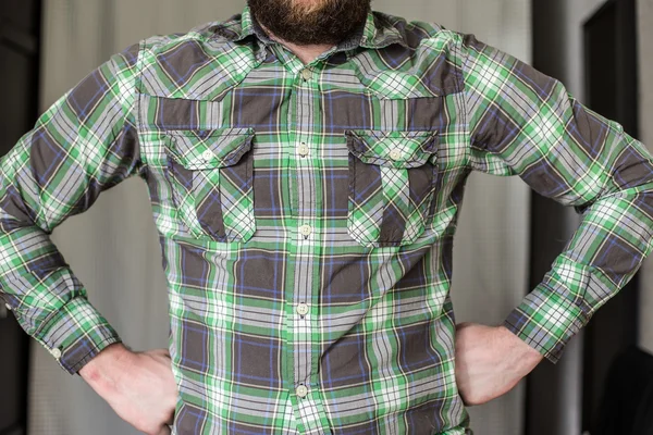 Bearded man in a checked shirt standing arms akimbo