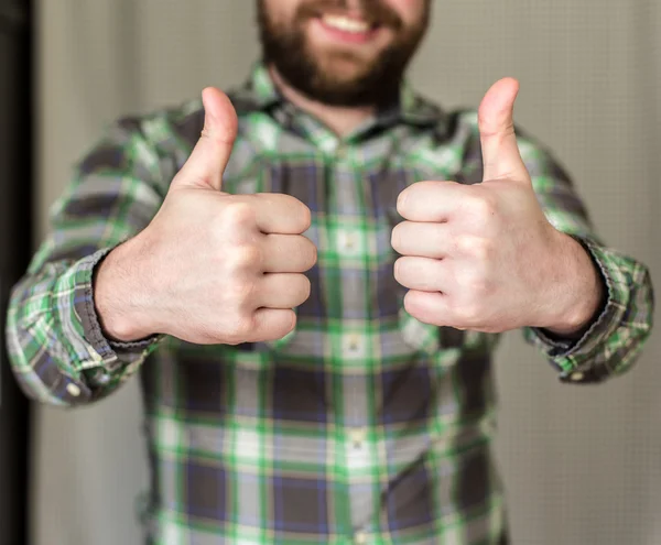 Smiling, bearded man in a checkered shirt has made two thumb up