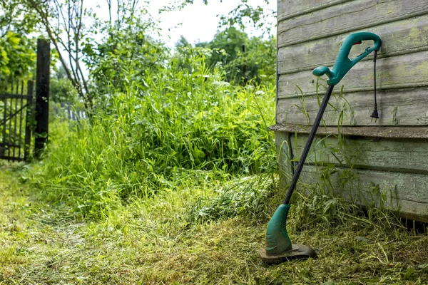 Electric grass trimmer stands in the garden near the house