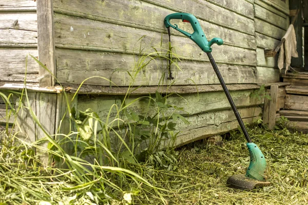 Electric grass trimmer stands in the garden near the house