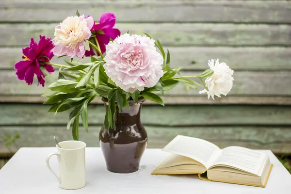 Vase the beautiful peonies, a cup with hot drink, the open book