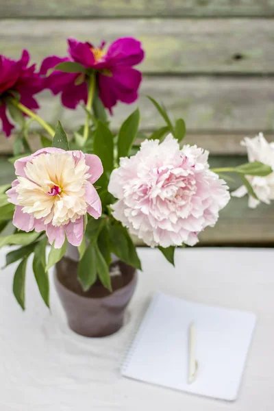 Vase of beautiful peony and memo pad with handle on a table cove