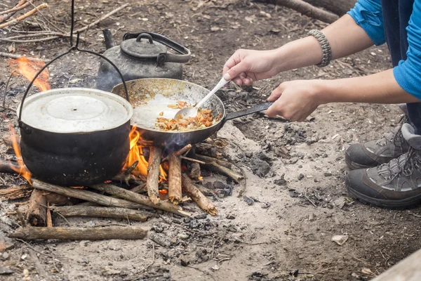 Tourist man fry food in a pan on the campfire