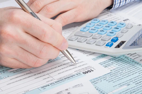 A man filling out USA Tax 1040 Form with dollars and calculator neat it