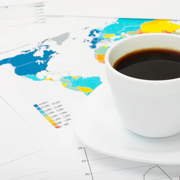 Coffee cup over world map and some financial documents next to it