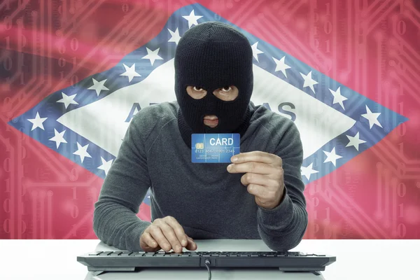 Dark-skinned hacker with USA states flag on background holding credit card - Arkansas