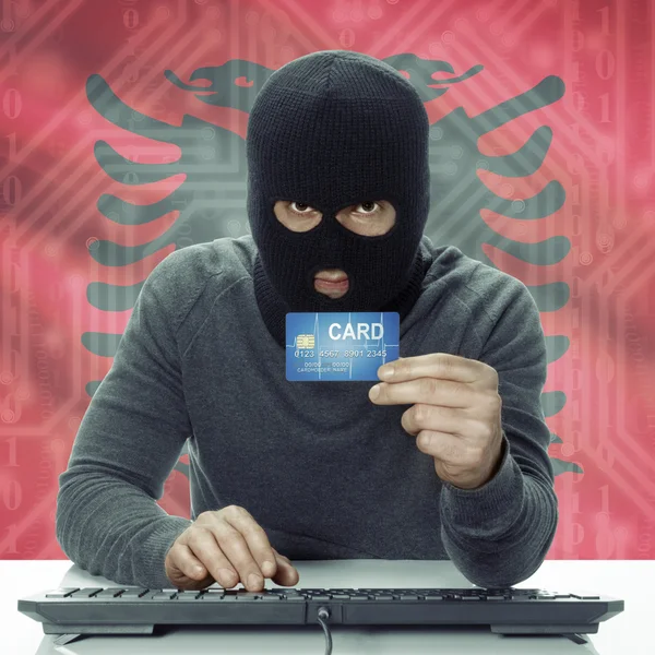 Dark-skinned hacker with flag on background holding credit card in hand - Albania