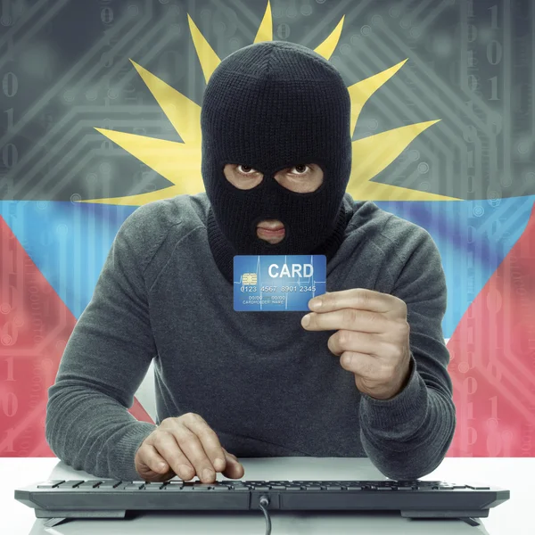 Dark-skinned hacker with flag on background holding credit card in hand - Antigua and Barbuda