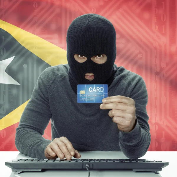 Dark-skinned hacker with flag on background holding credit card in hand - East Timor