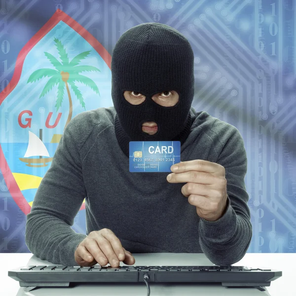 Dark-skinned hacker with flag on background holding credit card in hand - Guam