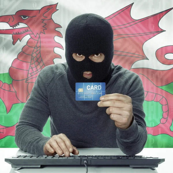 Dark-skinned hacker with flag on background holding credit card in hand - Wales