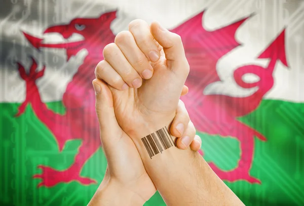 Barcode ID number on wrist and national flag on background - Wales