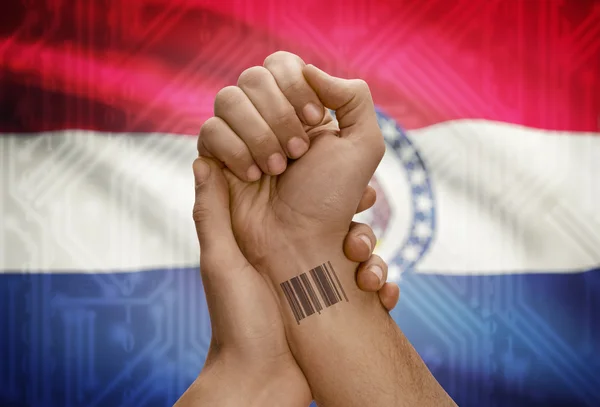 Barcode ID number on wrist of dark skinned person and USA states flags on background - Missouri