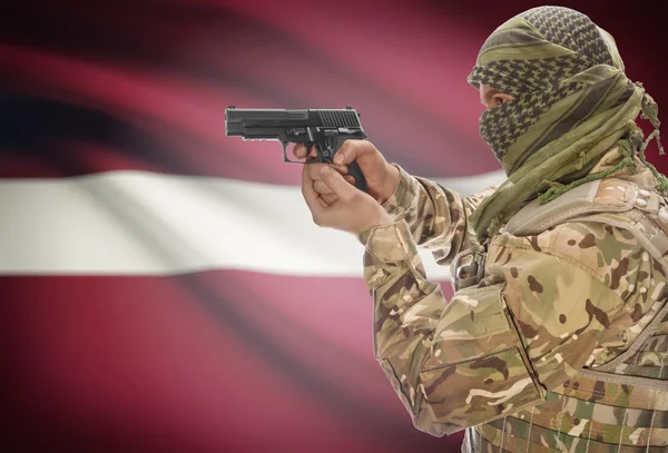 Male in muslim keffiyeh with gun in hand and national flag on background - Latvia
